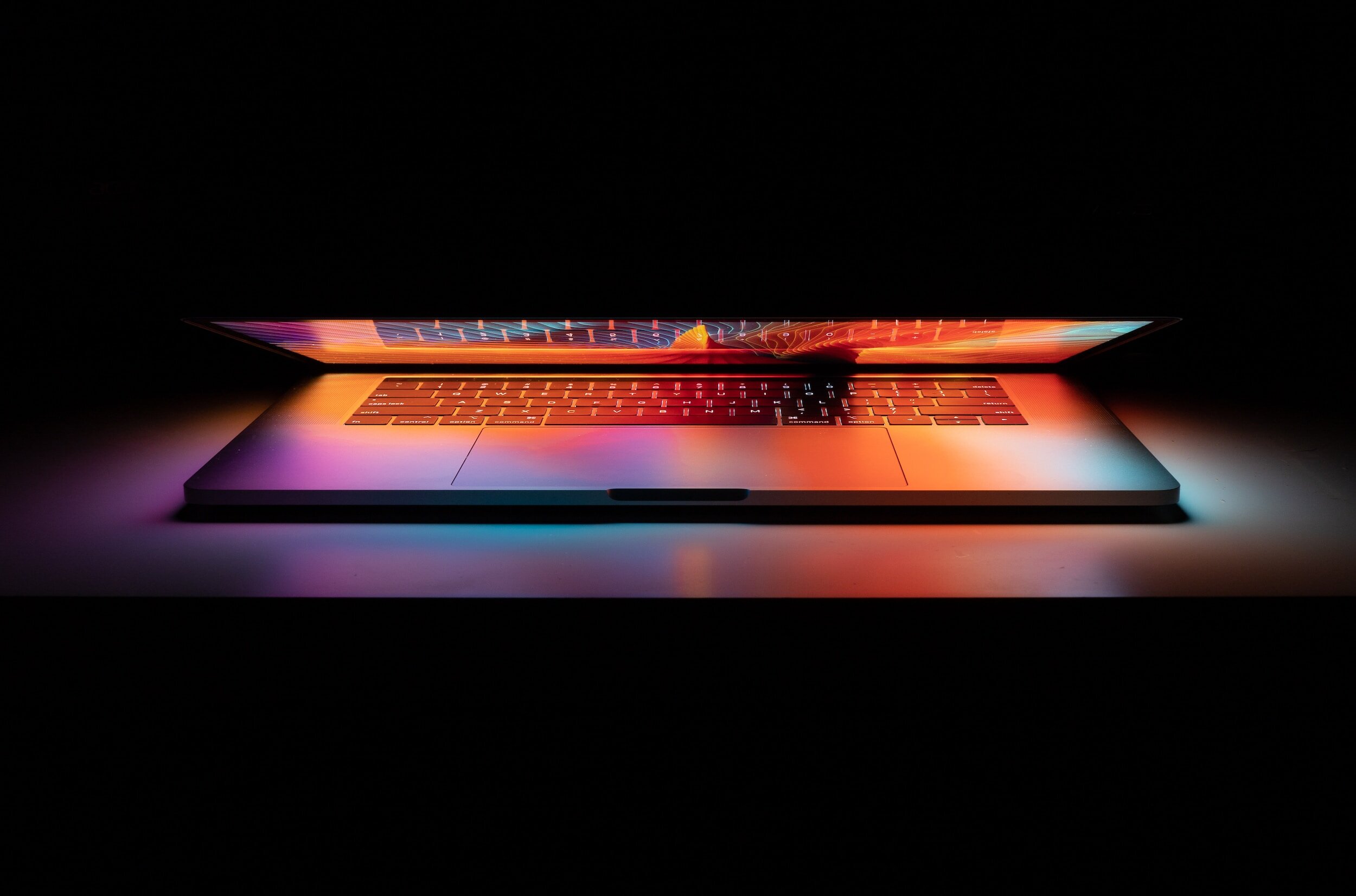 Laptop open in a dark room, screen glowing orange and blue