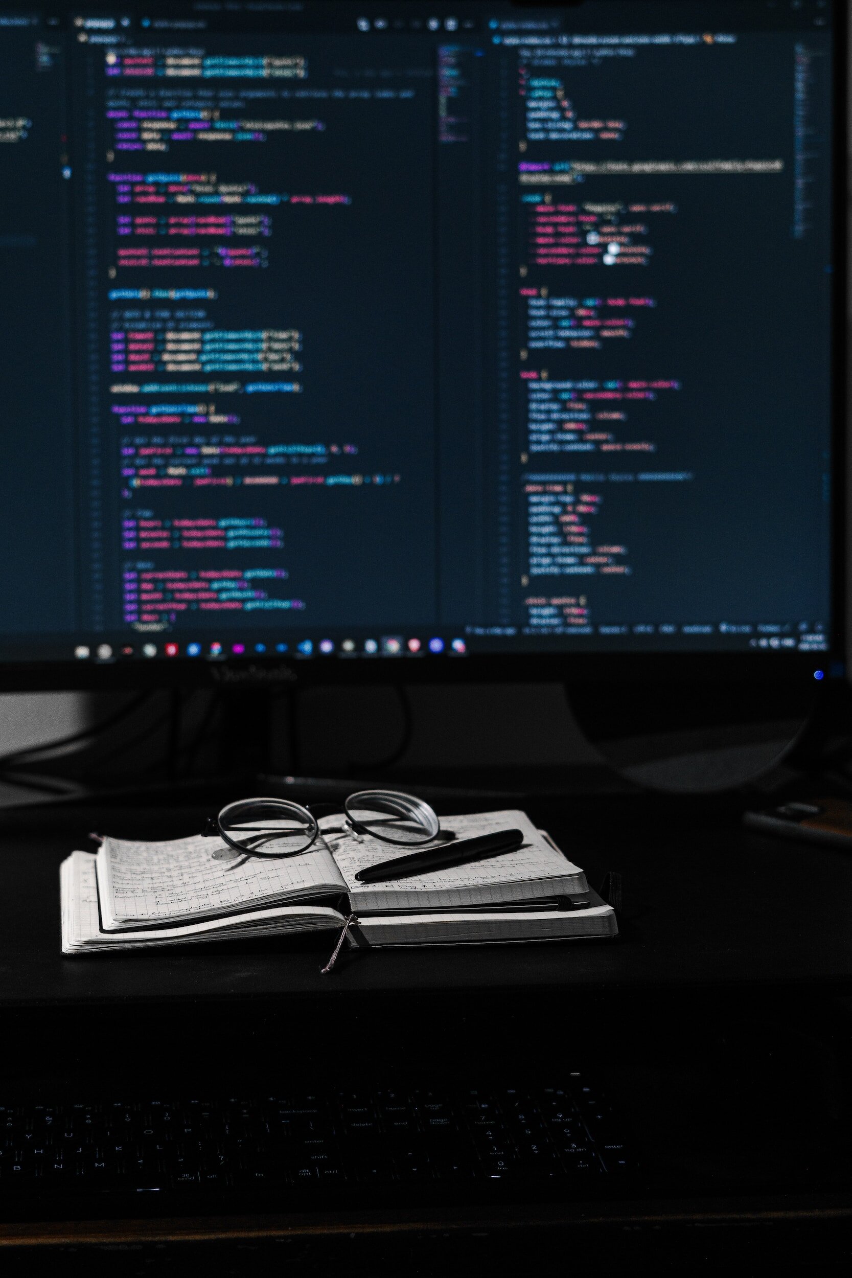 Notebook, glasses, and a monitor full of code